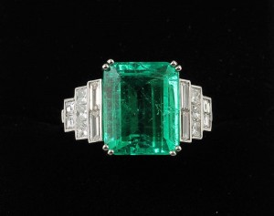 A VERY FINE QUALITY EMERALD RING, the trap cut emerald to stepped diamond shoulders. (20,000-25,000).