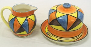 A Clarice Cliff cake dish and cover and jug, each estimated at 100-150.